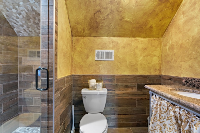 bathroom featuring vaulted ceiling, toilet, vanity, a shower with shower door, and tile walls