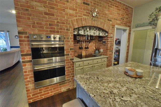 kitchen featuring dark hardwood / wood-style flooring, light stone counters, brick wall, stainless steel double oven, and black electric cooktop