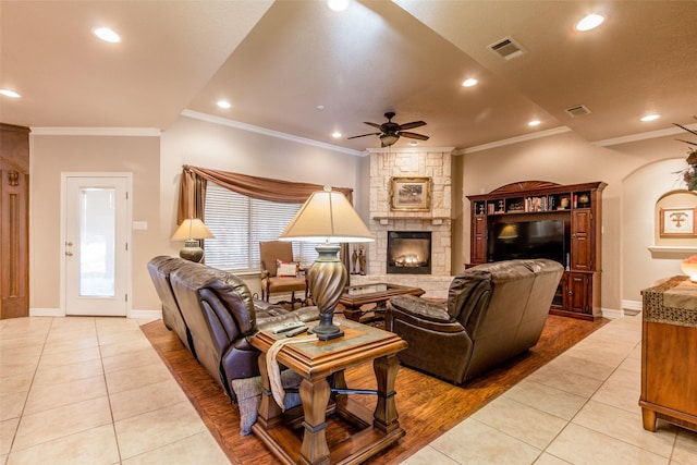 tiled living room featuring ornamental molding, a stone fireplace, and ceiling fan