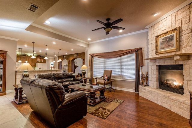 living room with crown molding, hardwood / wood-style flooring, ceiling fan, a fireplace, and a textured ceiling