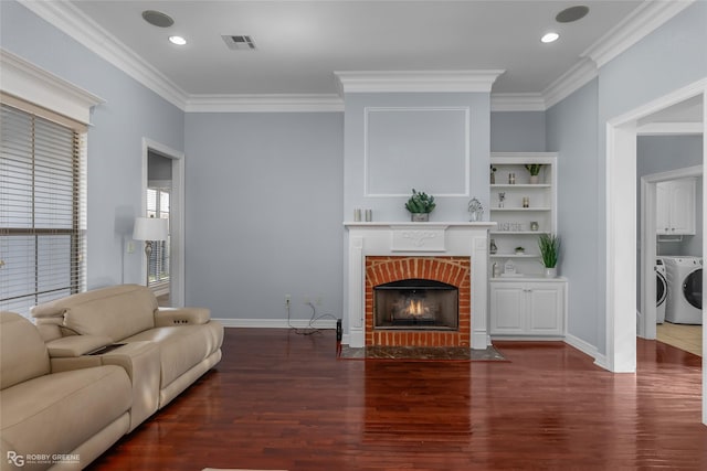 living room with crown molding, a brick fireplace, dark hardwood / wood-style floors, and washer and clothes dryer