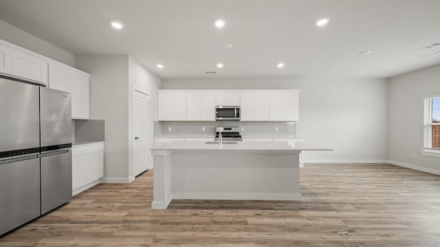 kitchen with white cabinetry, a center island with sink, stainless steel appliances, light hardwood / wood-style floors, and decorative backsplash