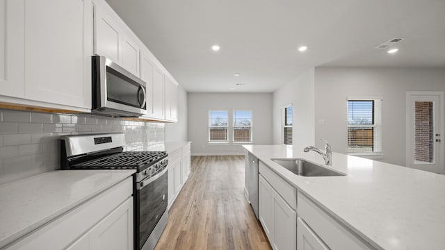 kitchen featuring sink, appliances with stainless steel finishes, white cabinetry, backsplash, and light wood-type flooring