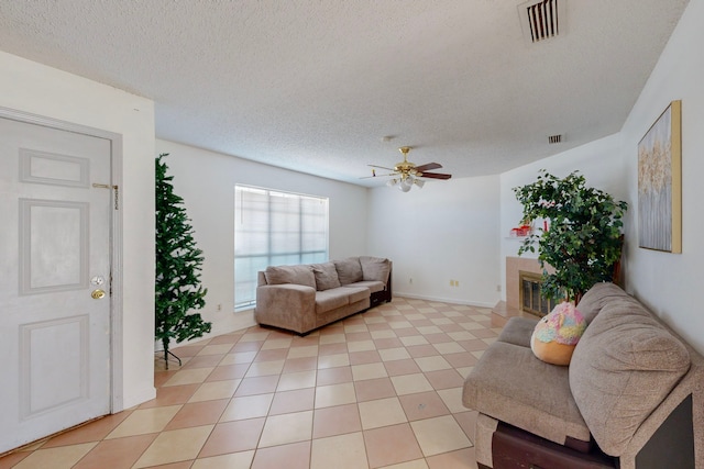 living room featuring a tile fireplace, a textured ceiling, ceiling fan, and light tile patterned flooring