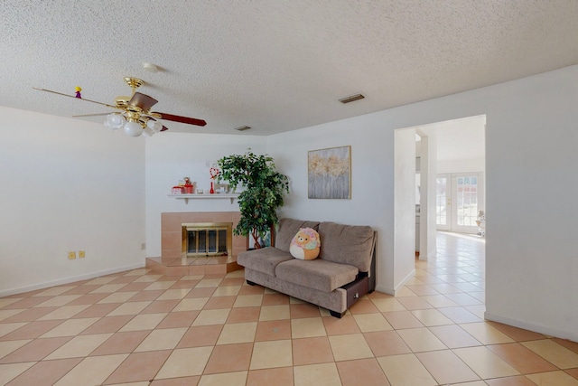 living room featuring ceiling fan, light tile patterned floors, a textured ceiling, and a tiled fireplace