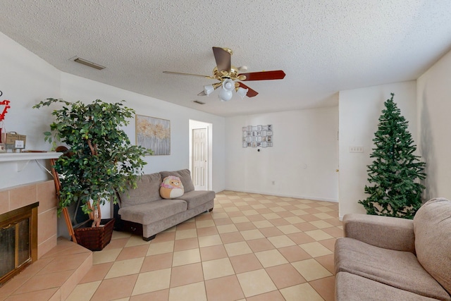 tiled living room with ceiling fan, a textured ceiling, and a tiled fireplace