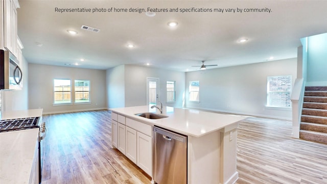 kitchen featuring white cabinetry, sink, stainless steel appliances, light hardwood / wood-style flooring, and a center island with sink