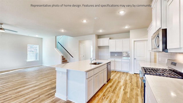 kitchen featuring sink, stainless steel appliances, backsplash, a center island with sink, and white cabinets