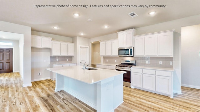 kitchen featuring sink, an island with sink, light hardwood / wood-style floors, white cabinetry, and stainless steel appliances