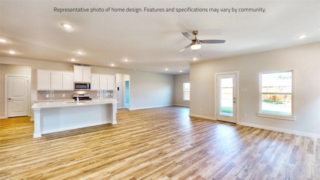 kitchen featuring white cabinets, decorative backsplash, an island with sink, appliances with stainless steel finishes, and light hardwood / wood-style floors