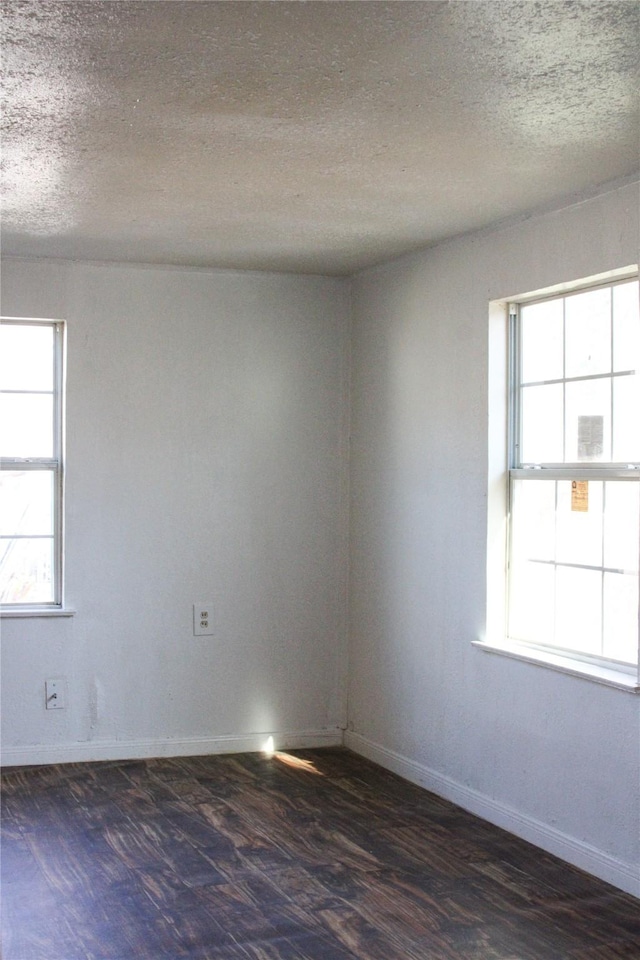 empty room with a textured ceiling, dark hardwood / wood-style flooring, and plenty of natural light