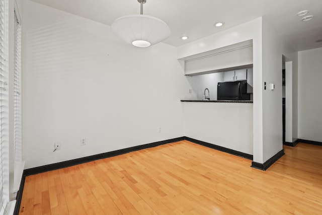 kitchen featuring pendant lighting, light hardwood / wood-style floors, black fridge, and sink