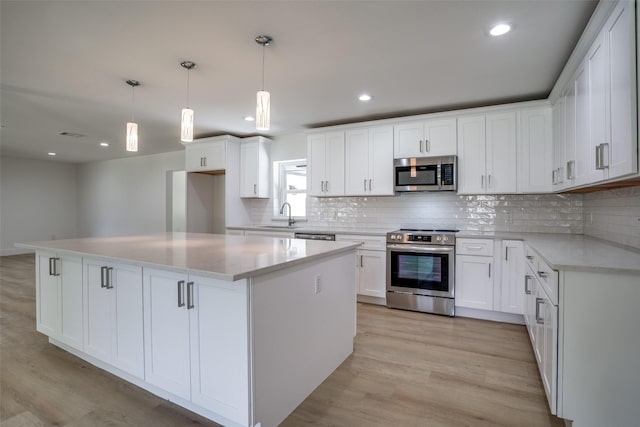 kitchen with a kitchen island, appliances with stainless steel finishes, pendant lighting, white cabinets, and light hardwood / wood-style floors