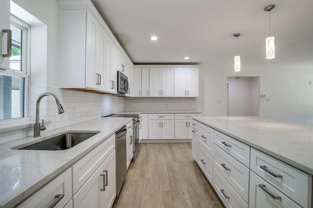 kitchen featuring appliances with stainless steel finishes, light stone counters, sink, pendant lighting, and white cabinetry