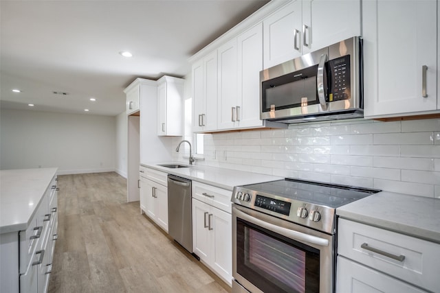 kitchen with white cabinetry, sink, light stone countertops, appliances with stainless steel finishes, and light wood-type flooring