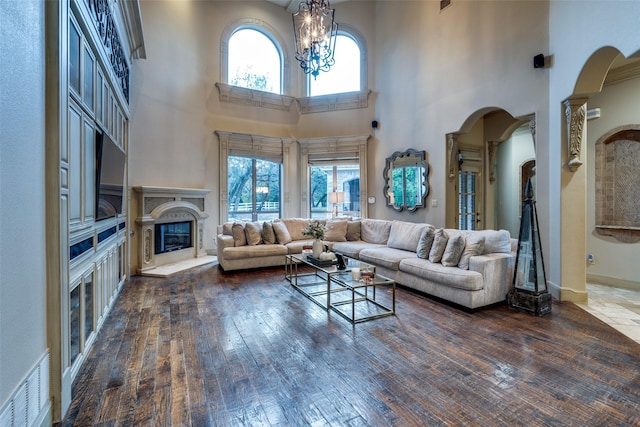 living room featuring dark hardwood / wood-style flooring, a towering ceiling, a notable chandelier, and a high end fireplace