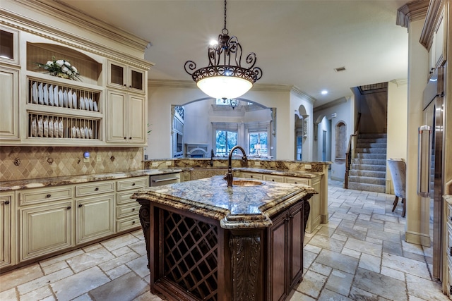 kitchen featuring sink, cream cabinets, light stone countertops, a center island with sink, and decorative light fixtures