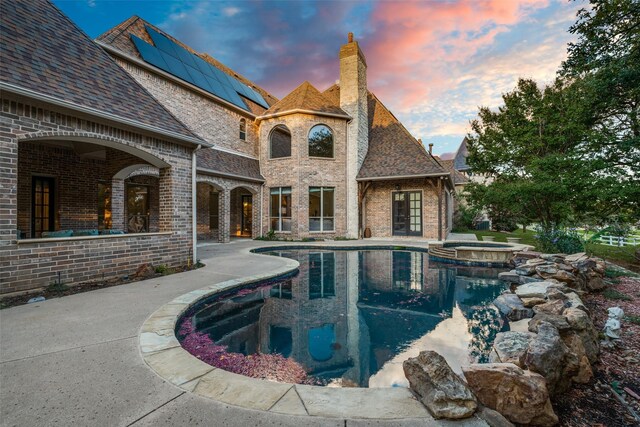 pool at dusk with an in ground hot tub