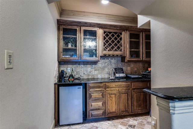 bar featuring sink, stainless steel refrigerator, backsplash, dark brown cabinetry, and ornamental molding