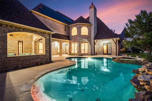 pool at dusk with an in ground hot tub and a patio