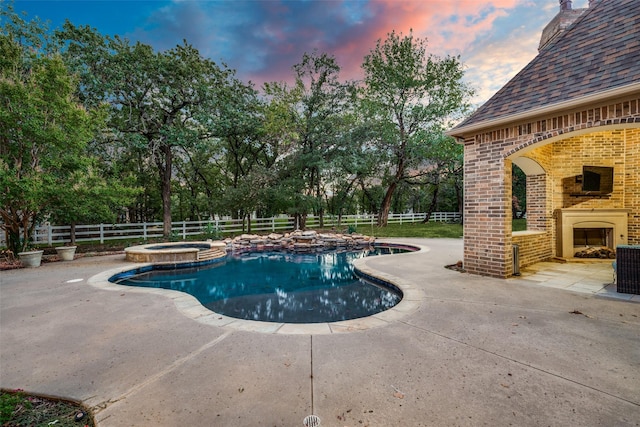 pool at dusk featuring an outdoor brick fireplace, an in ground hot tub, and a patio