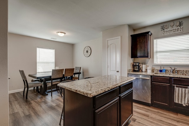 kitchen with sink, light stone counters, stainless steel dishwasher, a kitchen island, and light hardwood / wood-style floors