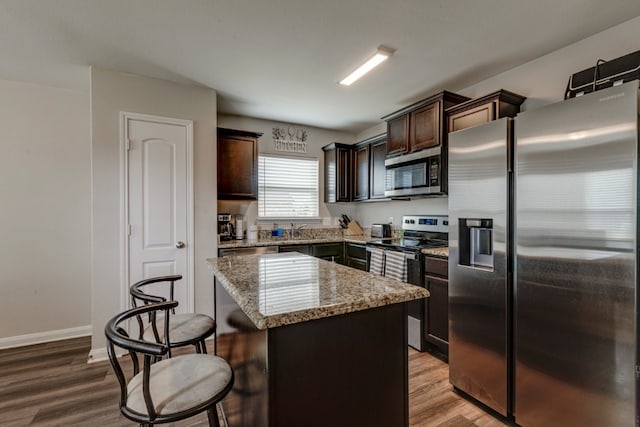 kitchen with hardwood / wood-style flooring, stone counters, appliances with stainless steel finishes, dark brown cabinets, and a center island