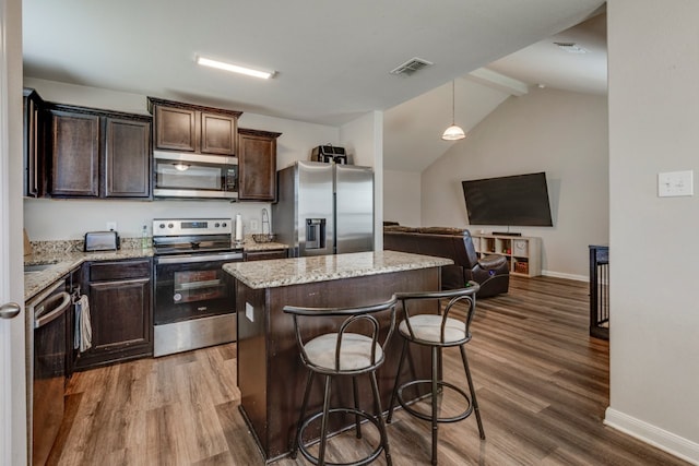 kitchen featuring hardwood / wood-style flooring, stainless steel appliances, a center island, light stone countertops, and decorative light fixtures