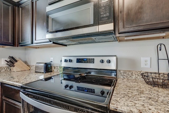 kitchen with appliances with stainless steel finishes, light stone counters, and dark brown cabinetry