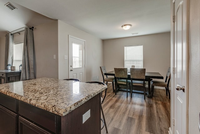 kitchen featuring dark wood-type flooring, a breakfast bar area, dark brown cabinetry, light stone counters, and a kitchen island