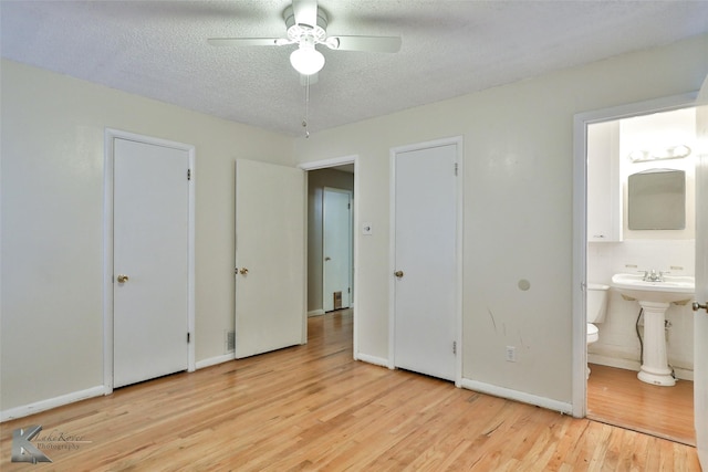 unfurnished bedroom featuring ensuite bath, ceiling fan, a textured ceiling, and light wood-type flooring