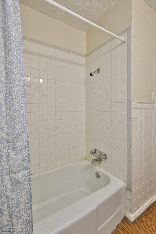 bathroom with hardwood / wood-style floors, a textured ceiling, tiled shower / bath combo, and tile walls