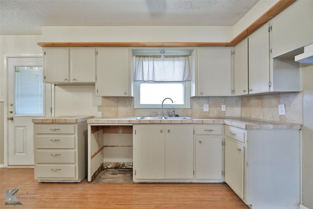 kitchen with white cabinetry, sink, tasteful backsplash, a textured ceiling, and light wood-type flooring