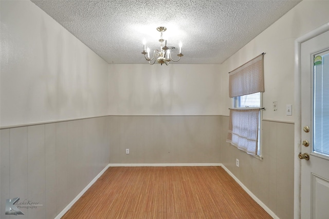 spare room with hardwood / wood-style floors, wooden walls, a textured ceiling, and a notable chandelier