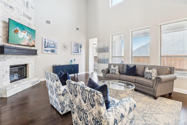 living room featuring a stone fireplace, plenty of natural light, a towering ceiling, and dark wood-type flooring