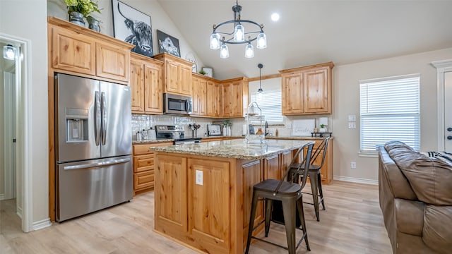 kitchen with appliances with stainless steel finishes, backsplash, light stone countertops, a kitchen island, and decorative light fixtures