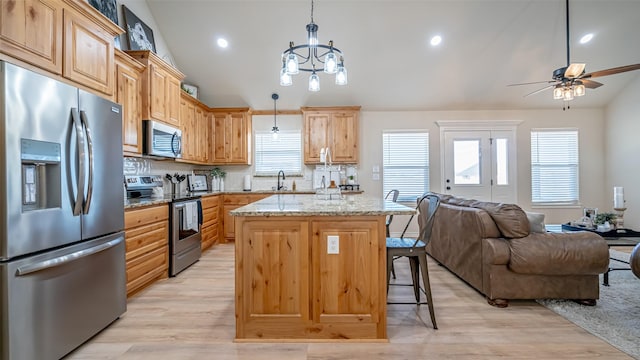 kitchen featuring vaulted ceiling, appliances with stainless steel finishes, pendant lighting, a center island, and light stone countertops