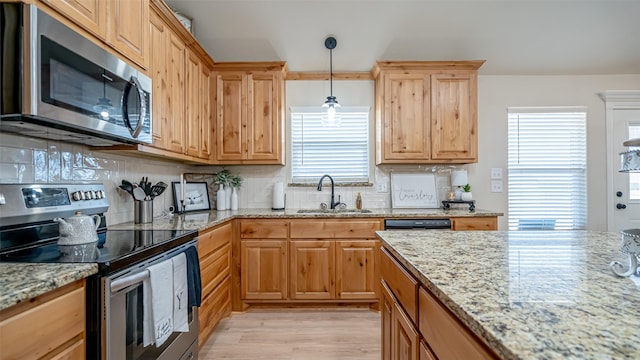 kitchen with sink, appliances with stainless steel finishes, backsplash, hanging light fixtures, and light stone counters