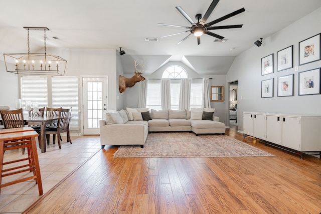 living room with ceiling fan with notable chandelier, lofted ceiling, and light hardwood / wood-style flooring