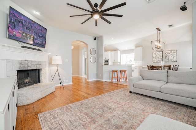 living room with ceiling fan with notable chandelier, light hardwood / wood-style flooring, and a stone fireplace