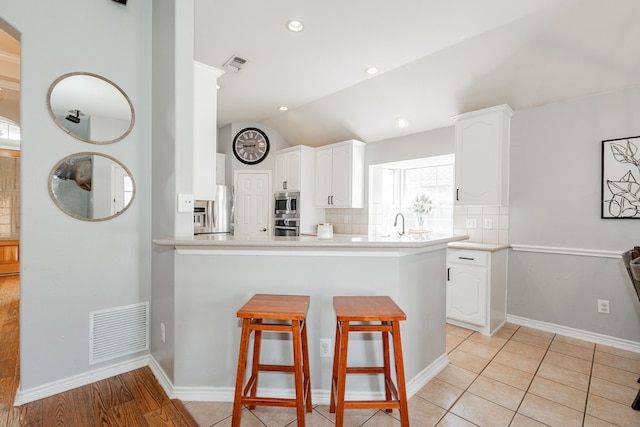 kitchen with kitchen peninsula, backsplash, white cabinetry, and vaulted ceiling