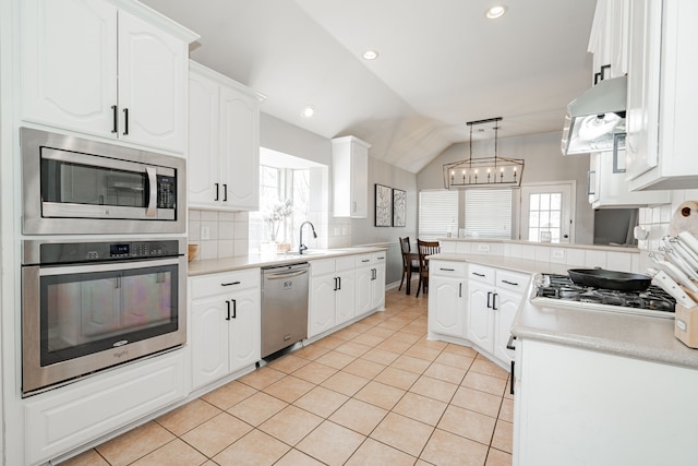 kitchen with stainless steel appliances, vaulted ceiling, exhaust hood, white cabinets, and hanging light fixtures