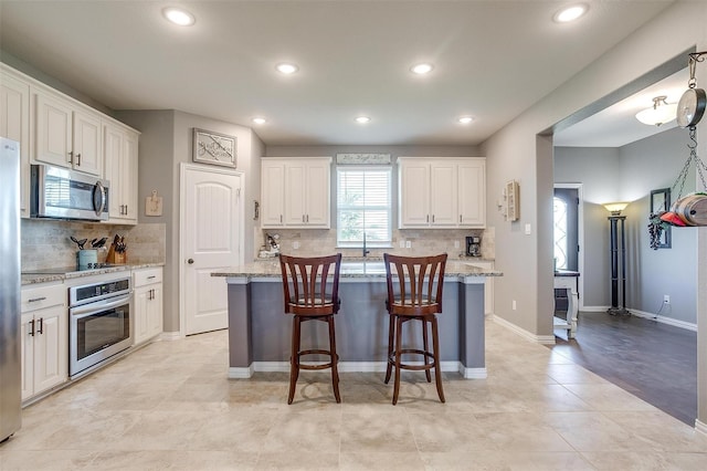 kitchen with a center island with sink, light stone counters, appliances with stainless steel finishes, a kitchen bar, and white cabinetry