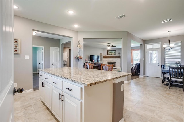 kitchen featuring light stone countertops, a center island, hanging light fixtures, white cabinets, and ceiling fan with notable chandelier