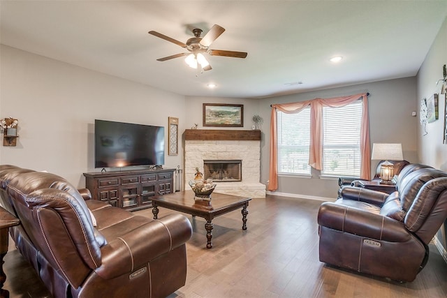 living room with wood-type flooring, a stone fireplace, and ceiling fan