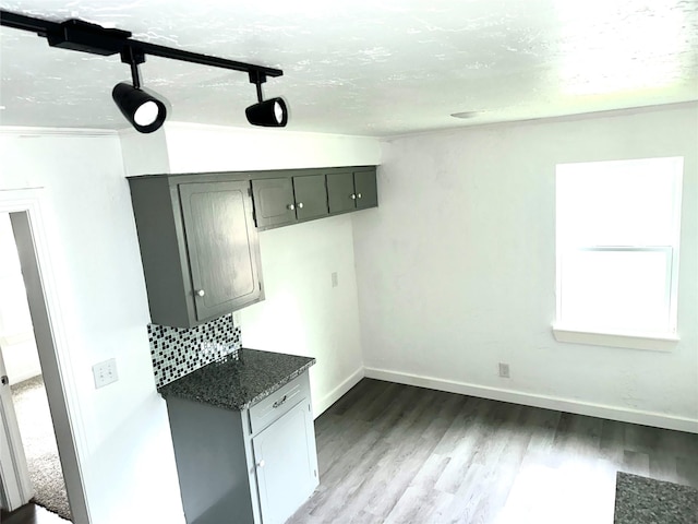 kitchen with backsplash, rail lighting, dark stone counters, wood-type flooring, and gray cabinets