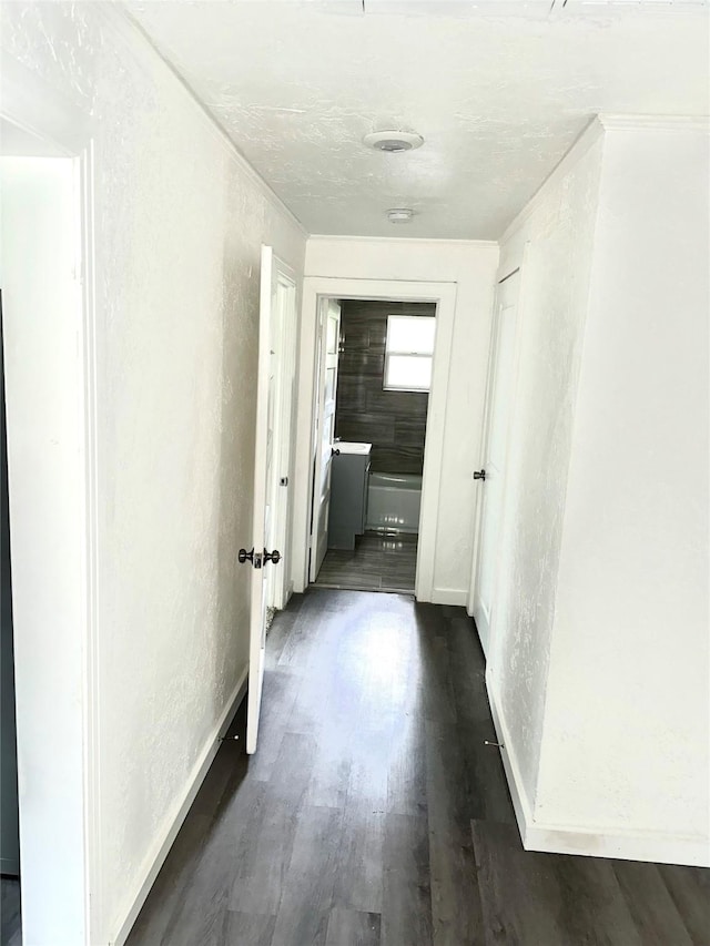 hallway featuring dark wood-style floors, baseboards, and a textured wall