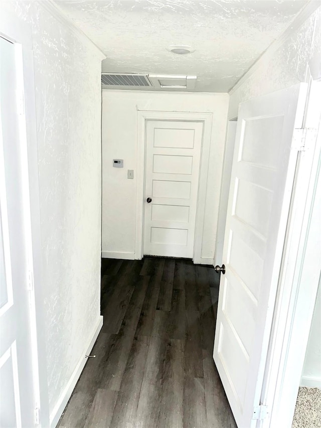 hall with dark wood finished floors, visible vents, a textured wall, attic access, and baseboards