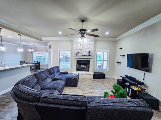 tiled living room with a wealth of natural light, crown molding, a fireplace, and ceiling fan with notable chandelier