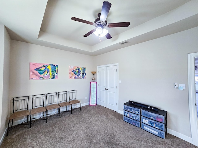 misc room with a tray ceiling, ceiling fan, and dark colored carpet